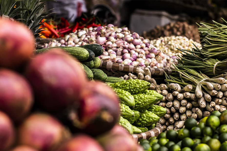 Market with fresh fruits and vegetables, including mangoes, cucumbers, onions, lemons and lemongrass.
