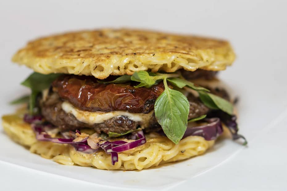 Unique hamburger with ramen noodle buns, tomatoes, and basil.