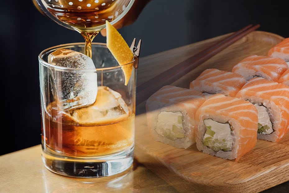 Cocktail and sushi on a wooden table, a casual meal with contrasting flavors.