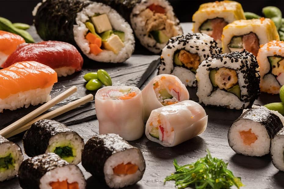 An assortment of sushi on a black platter, with chopsticks and wasabi