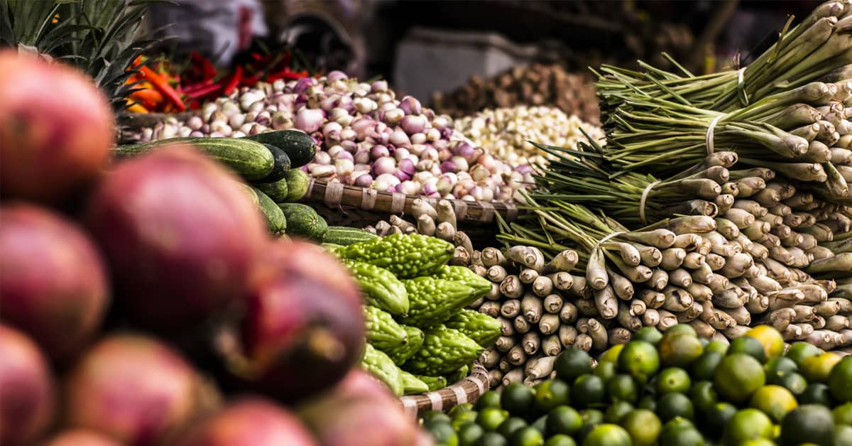 Marché avec des fruits et légumes frais, dont des mangues, des concombres, des oignons, des citrons et du citronnelle.